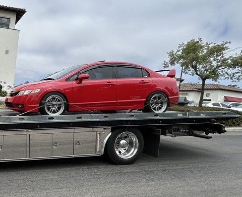 Red sedan on the deck of a flatbed tow truck