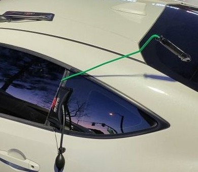 Car lockout at night: an air wedge and a long-reach tool in the door of a white coupe