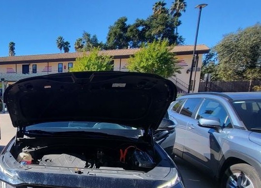 SUV with the hood up and red jumper clamps on the battery in a parking lot